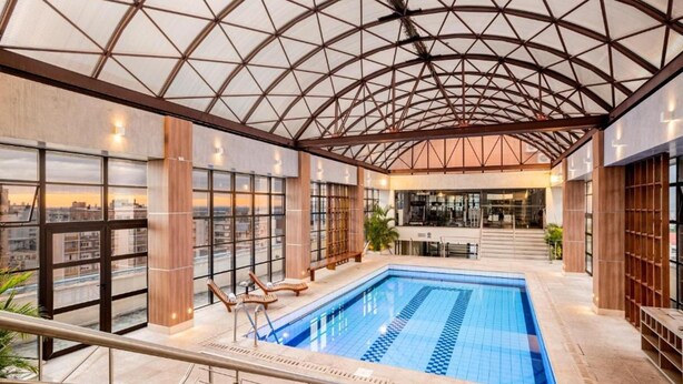 A modern indoor swimming pool with a glass ceiling, wooden columns, and a city view. - Piazza Navona Porto Alegre by Intercity (Porto Alegre)
