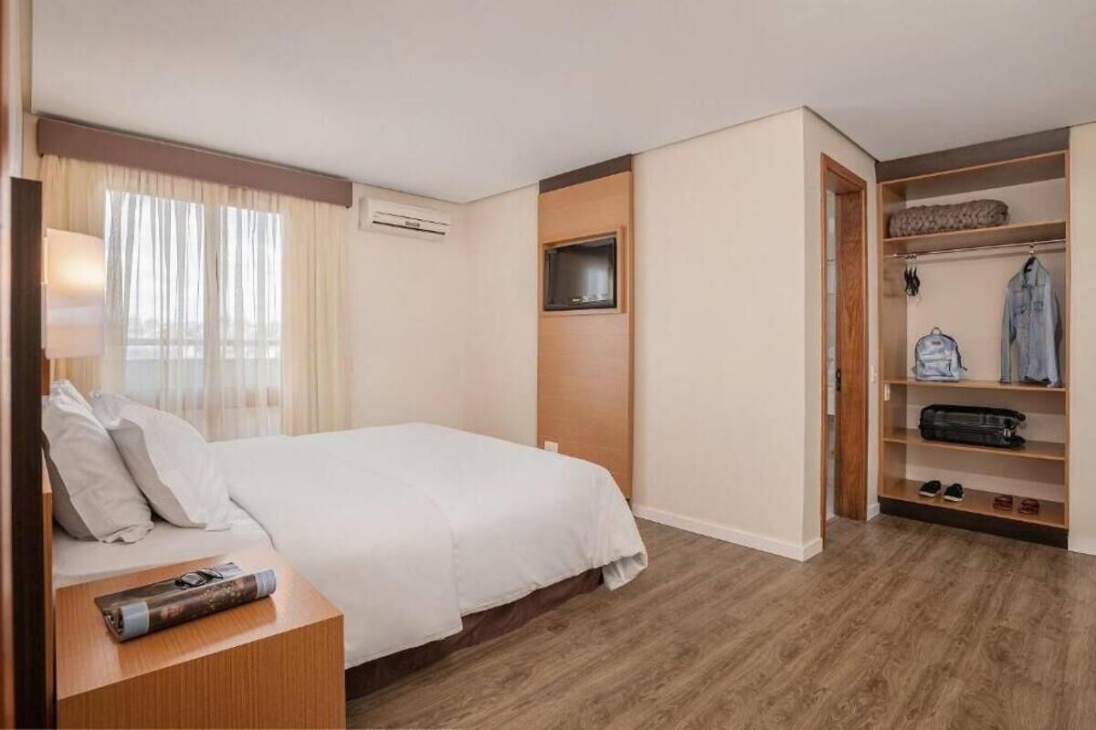 Ein Hotelzimmer mit Bett, Wandfernseher, Schrank und einem Fenster mit Vorhängen.