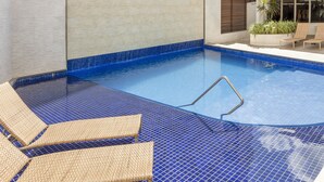 A swimming pool with blue tiles, a metal ladder, and wicker lounge chairs. - Internacional Palace Hotel (Recife)