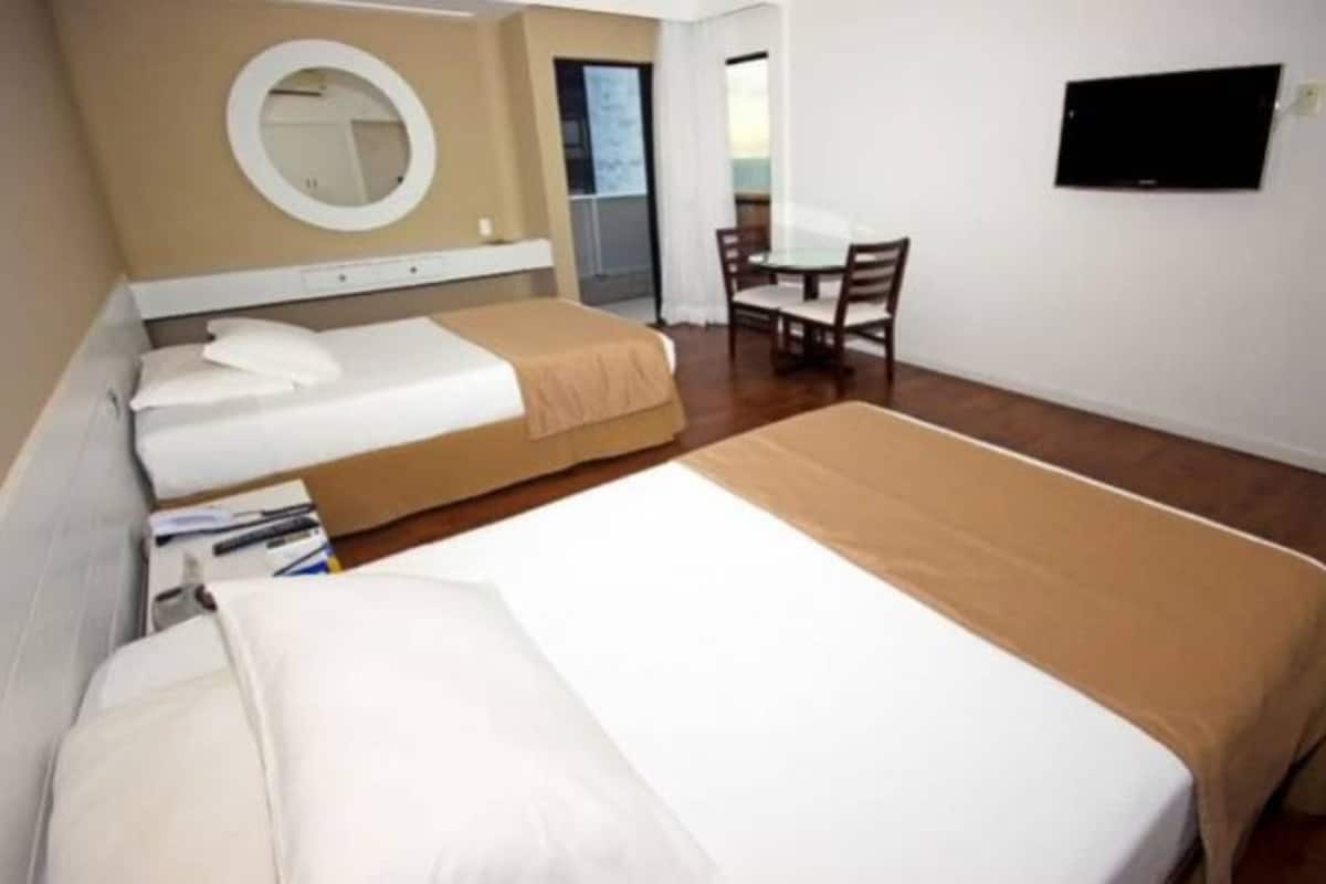 Habitación de hotel con dos camas, un espejo redondo, una mesita pequeña y un televisor en la pared.