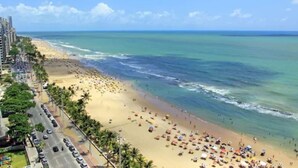 A beach with a road running parallel to it, lined with palm trees and buildings. - Internacional Palace Hotel (Recife)