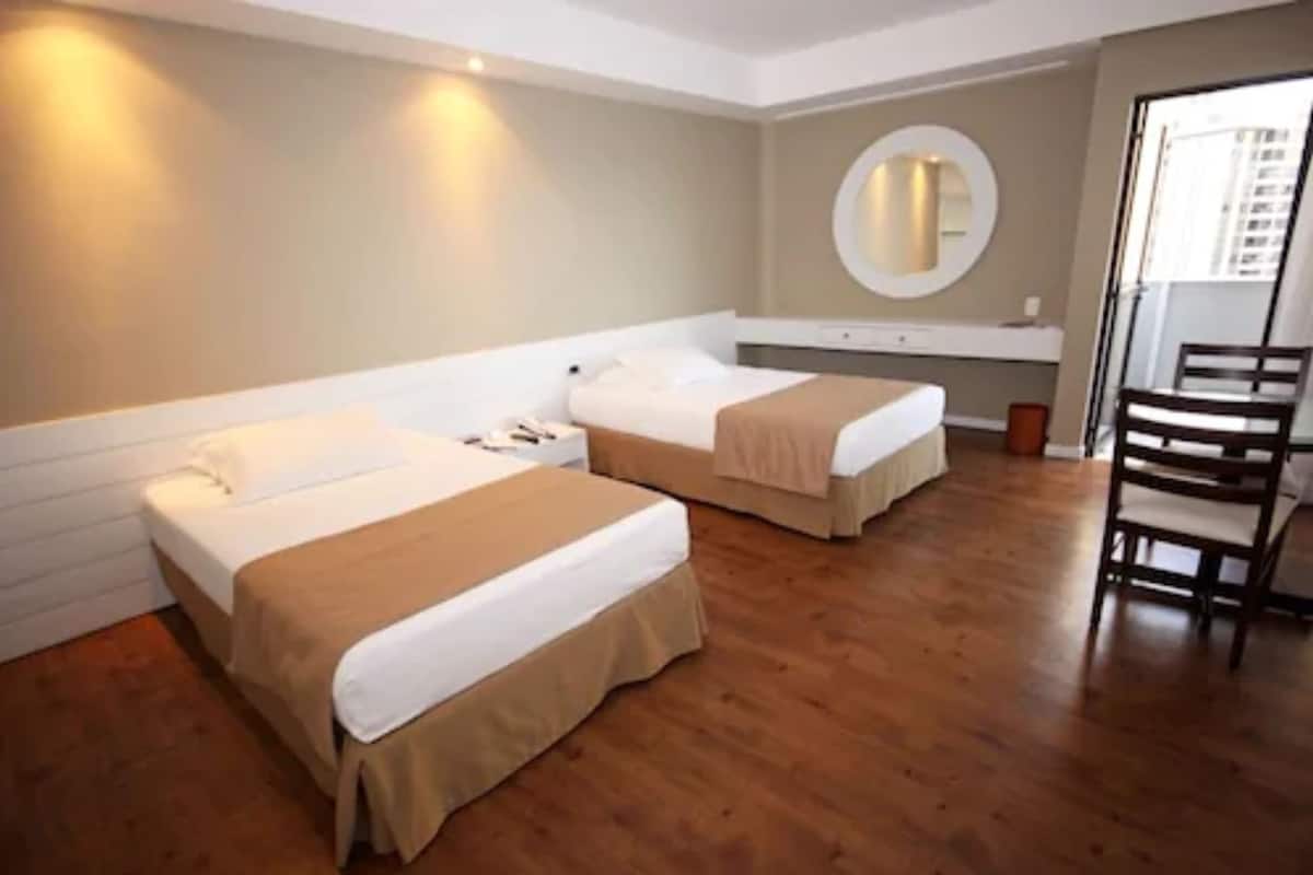 Habitación de hotel con dos camas, suelo de madera, un espejo redondo y una silla.