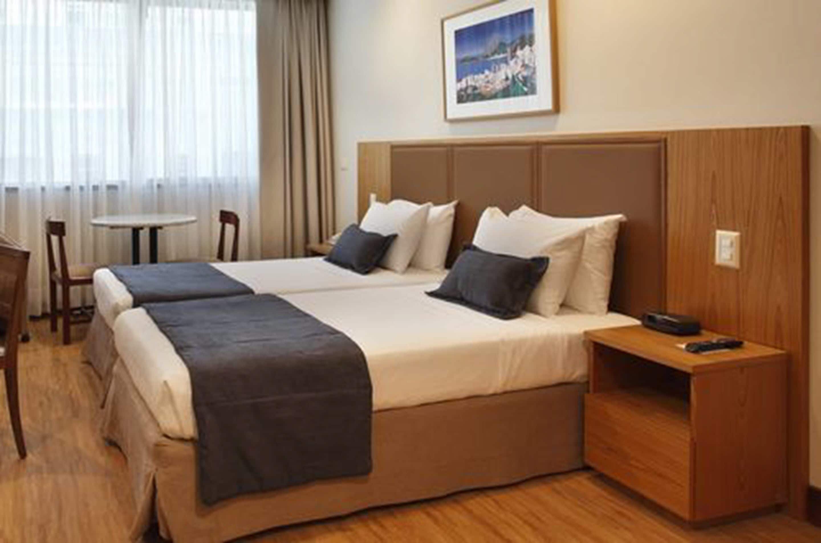 A hotel room with two beds, a small table, and a chair.