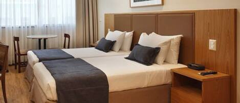 A hotel room with two beds, a small table, and a chair.