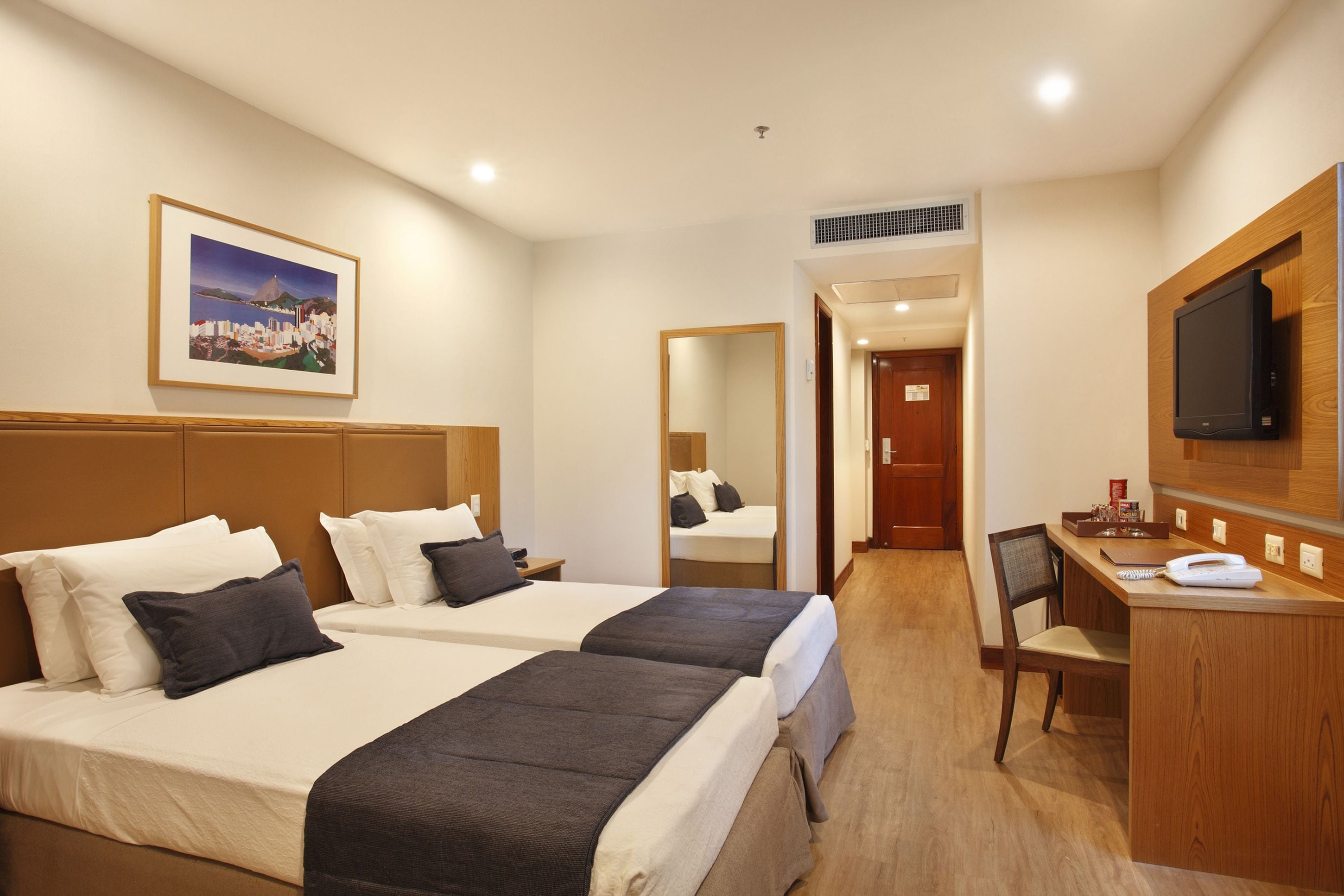 A hotel room with two beds, a desk, a chair, a television, and a framed picture on the wall.