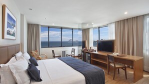 Una habitación de hotel con una cama grande, un escritorio, un televisor y vista al océano.