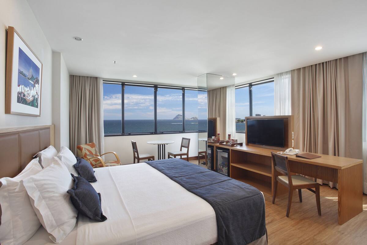 A hotel room with a large bed, a desk, a television, and a view of the ocean.