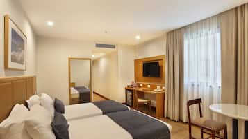 A hotel room with two beds, a desk, a chair, a TV, and a window with curtains.