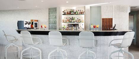 A modern bar area with a granite countertop, white metal chairs, and a variety of liquor bottles.