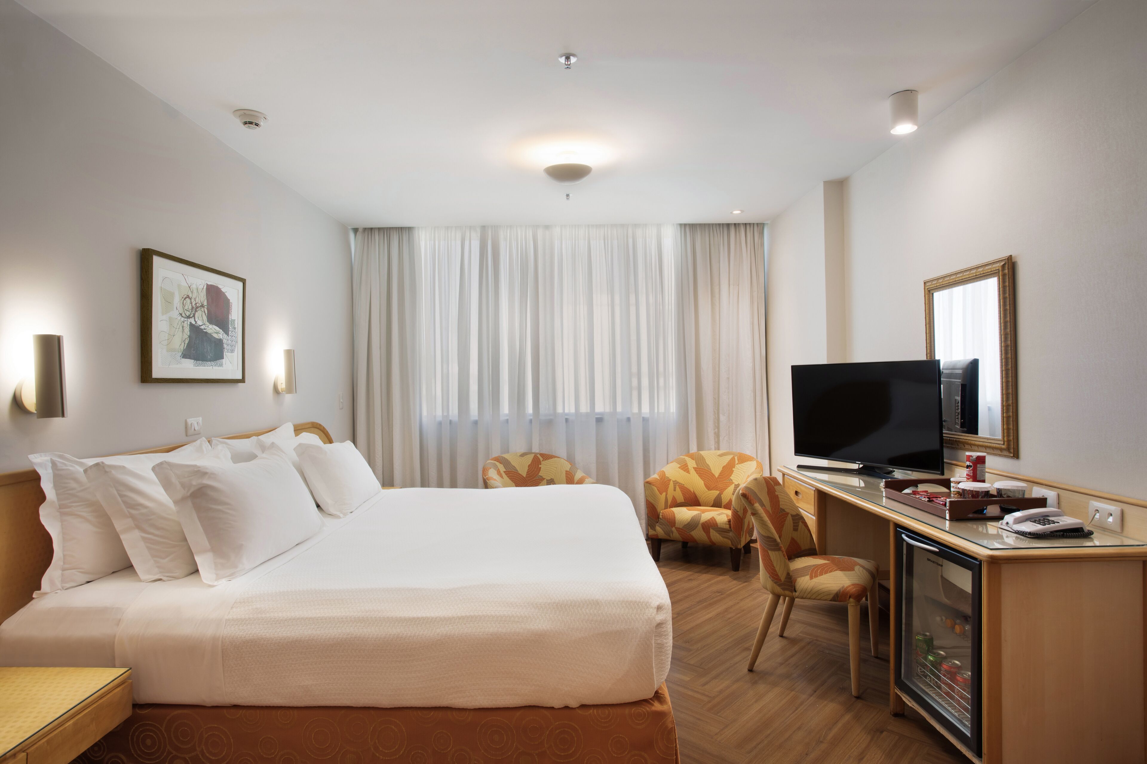 Une chambre d’hôtel comprenant un lit, un bureau avec une télévision, une chaise et un mini-bar.