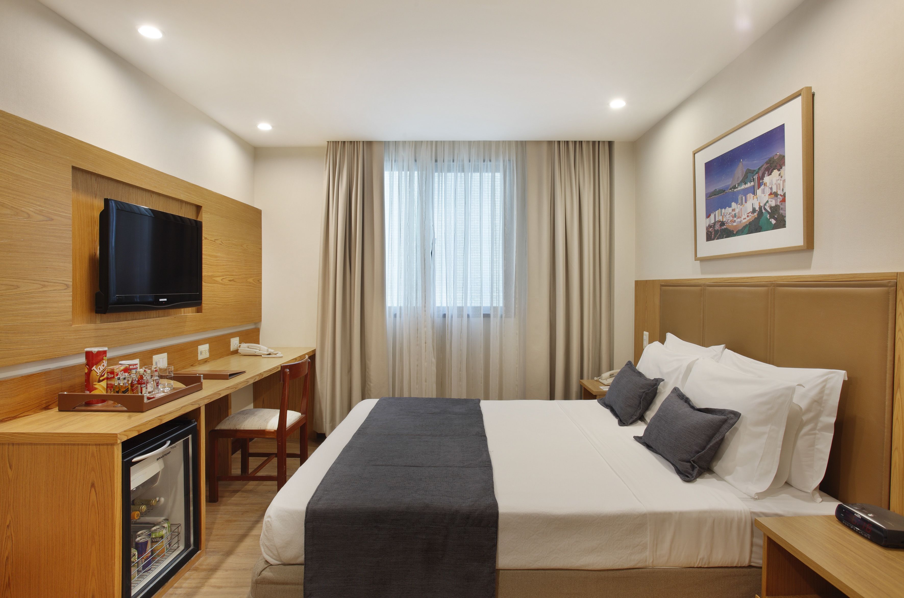 Habitación de hotel con cama, escritorio, televisión, minibar y ventana con cortinas.