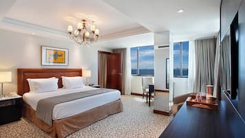 Habitación de hotel con una cama grande, un escritorio, un televisor y vista al océano.