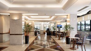Un vestíbulo de hotel con suelo de diseño geométrico, zonas de estar y plantas en macetas.