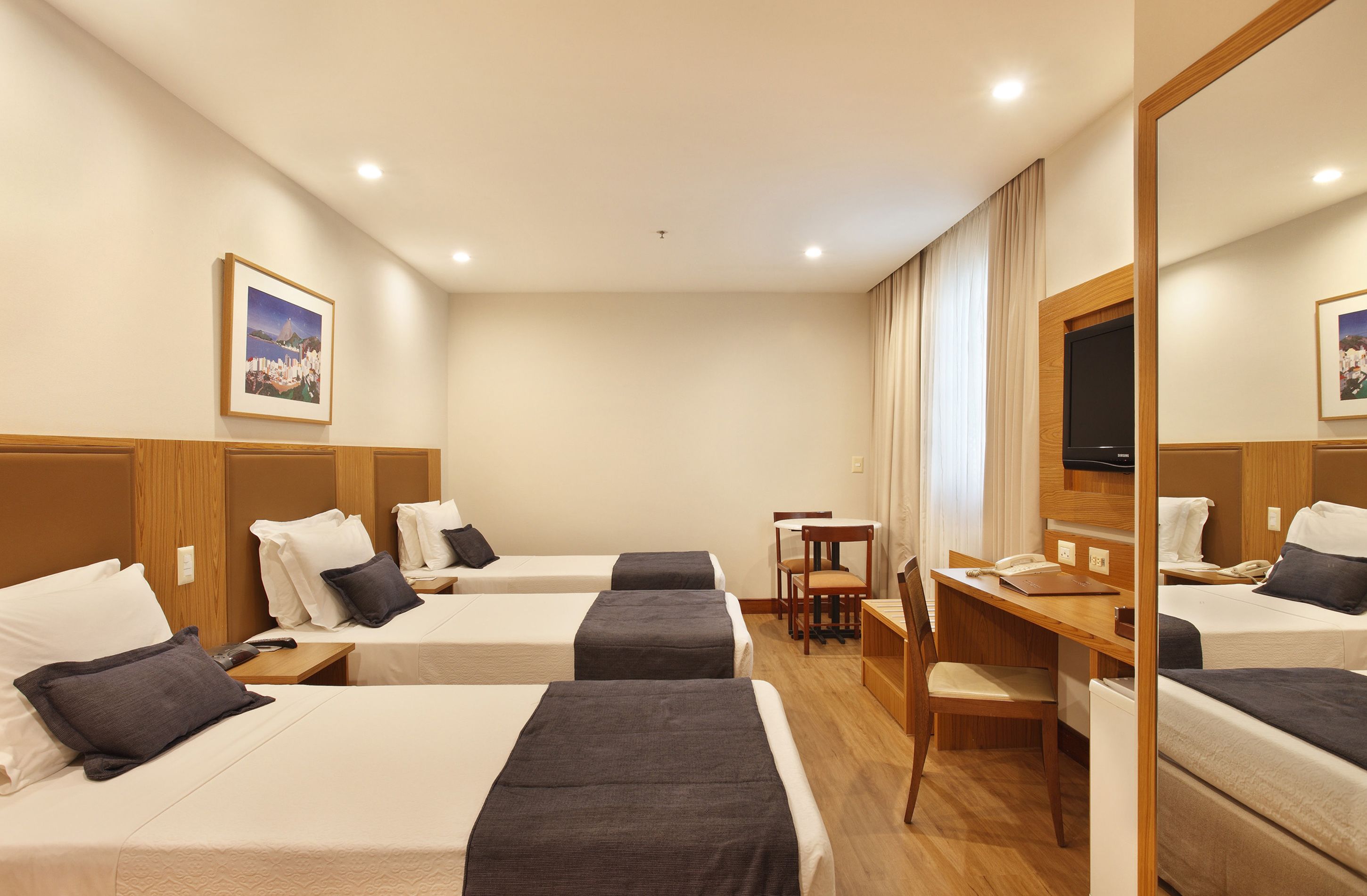 Habitación de hotel con tres camas individuales, un escritorio, una silla y un televisor.