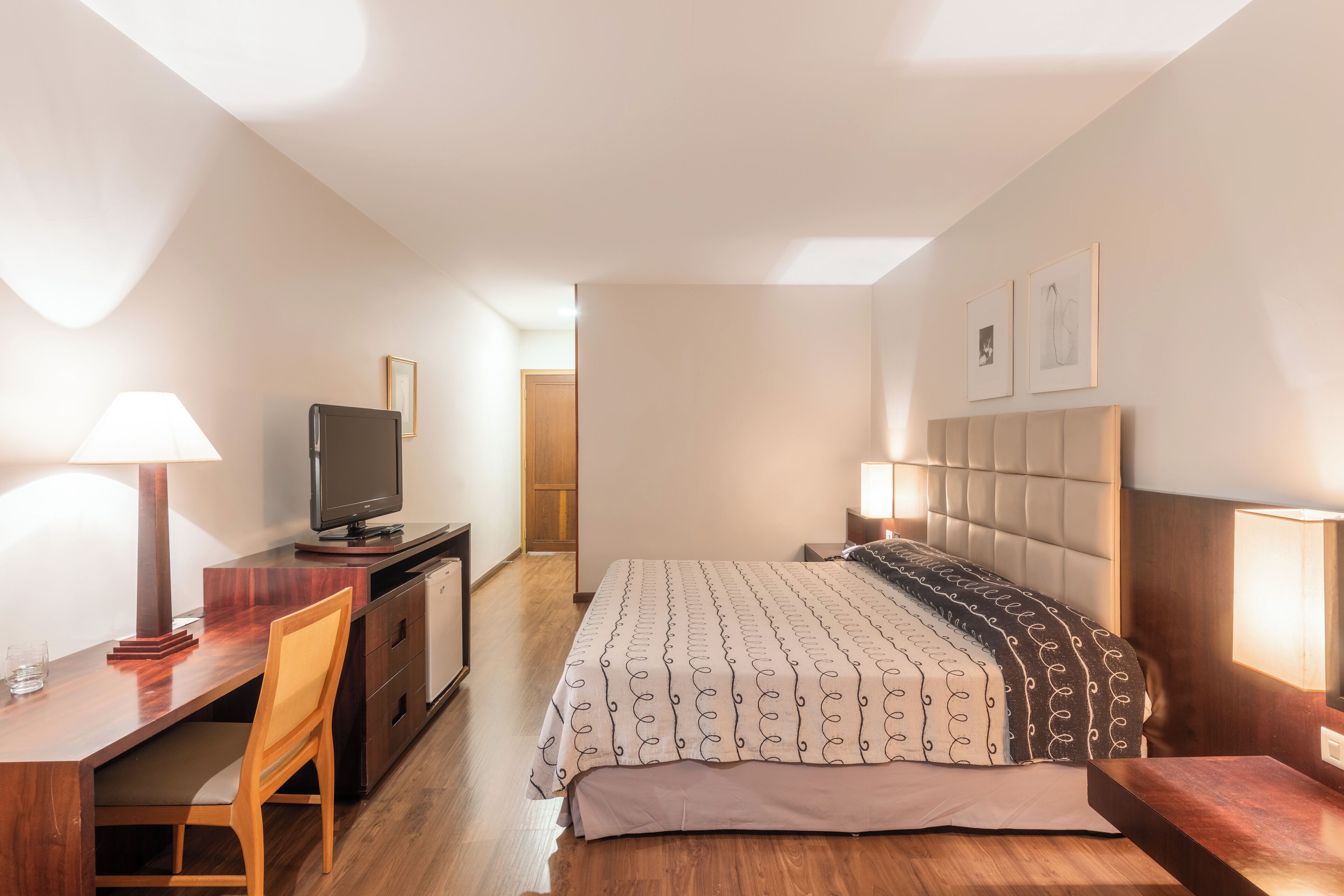 Un dormitorio con cama, mesitas de noche, escritorio, televisión y una silla.