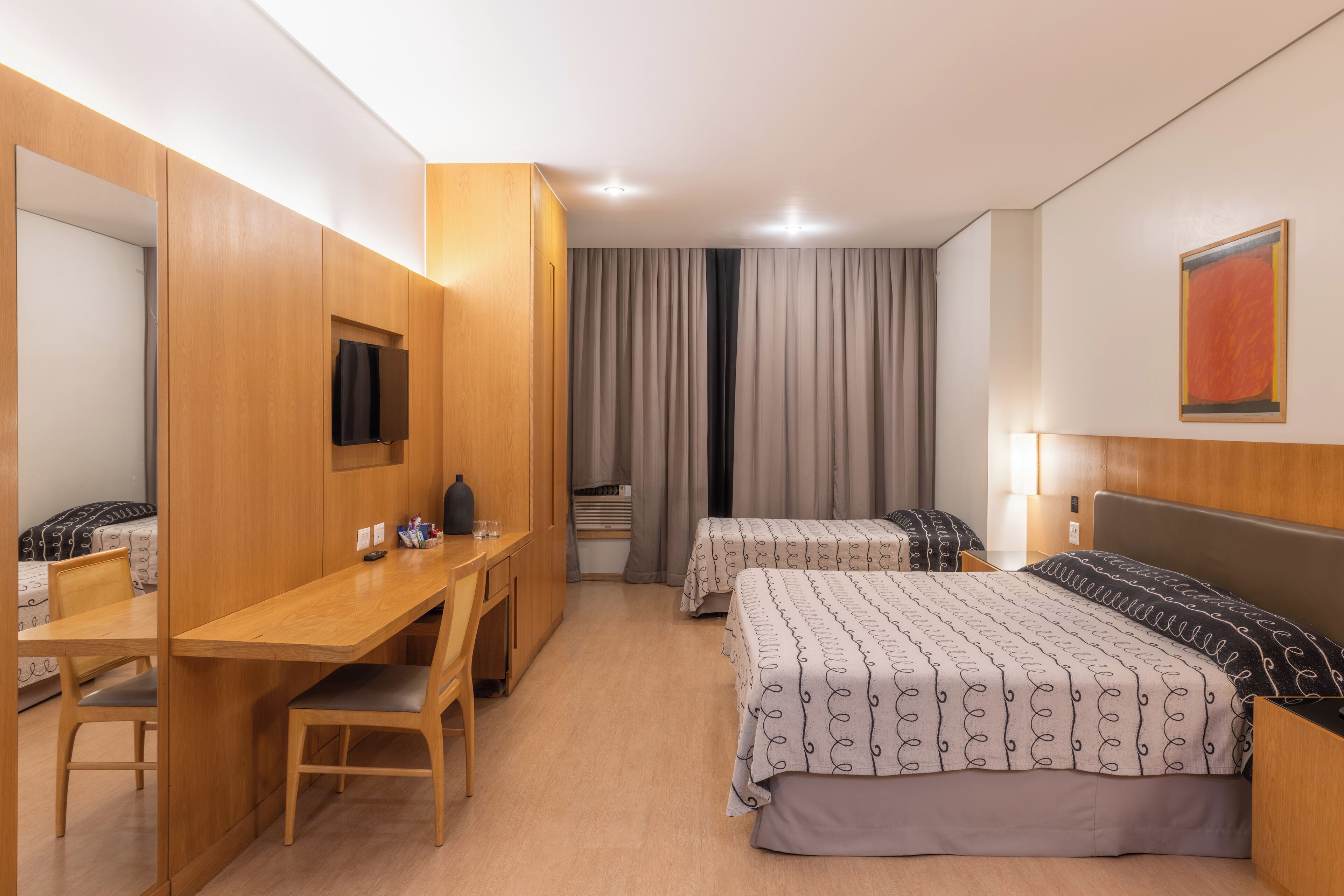Una habitación de hotel con un escritorio de madera, dos camas, un televisor y un espejo grande.
