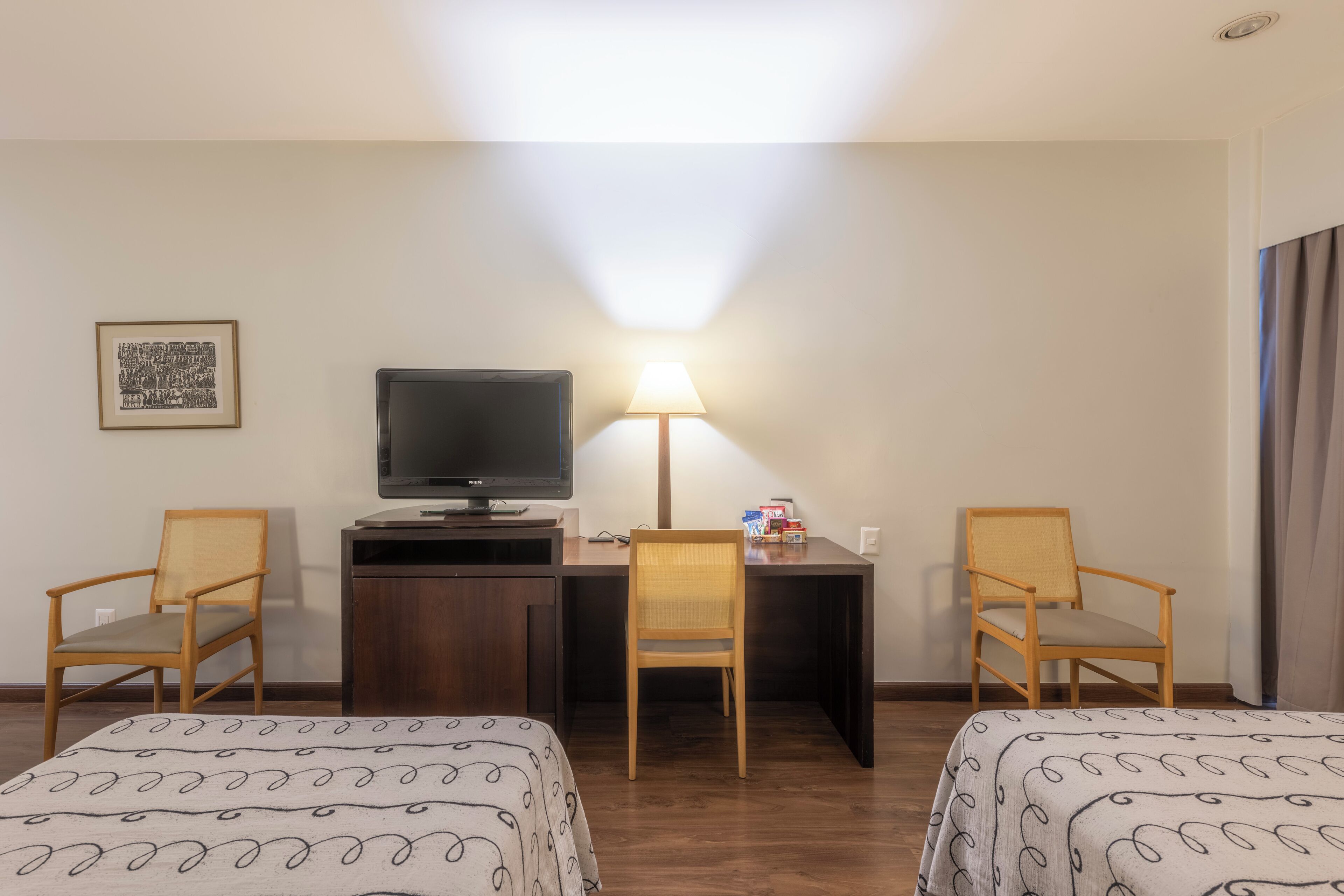 Une chambre d’hôtel avec deux lits, un bureau avec une télévision, une lampe et deux chaises.