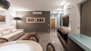 Una sala moderna con un sofá, mesa de comedor y sillas. Hay cuadros en la pared, un televisor y un aparador de vidrio.