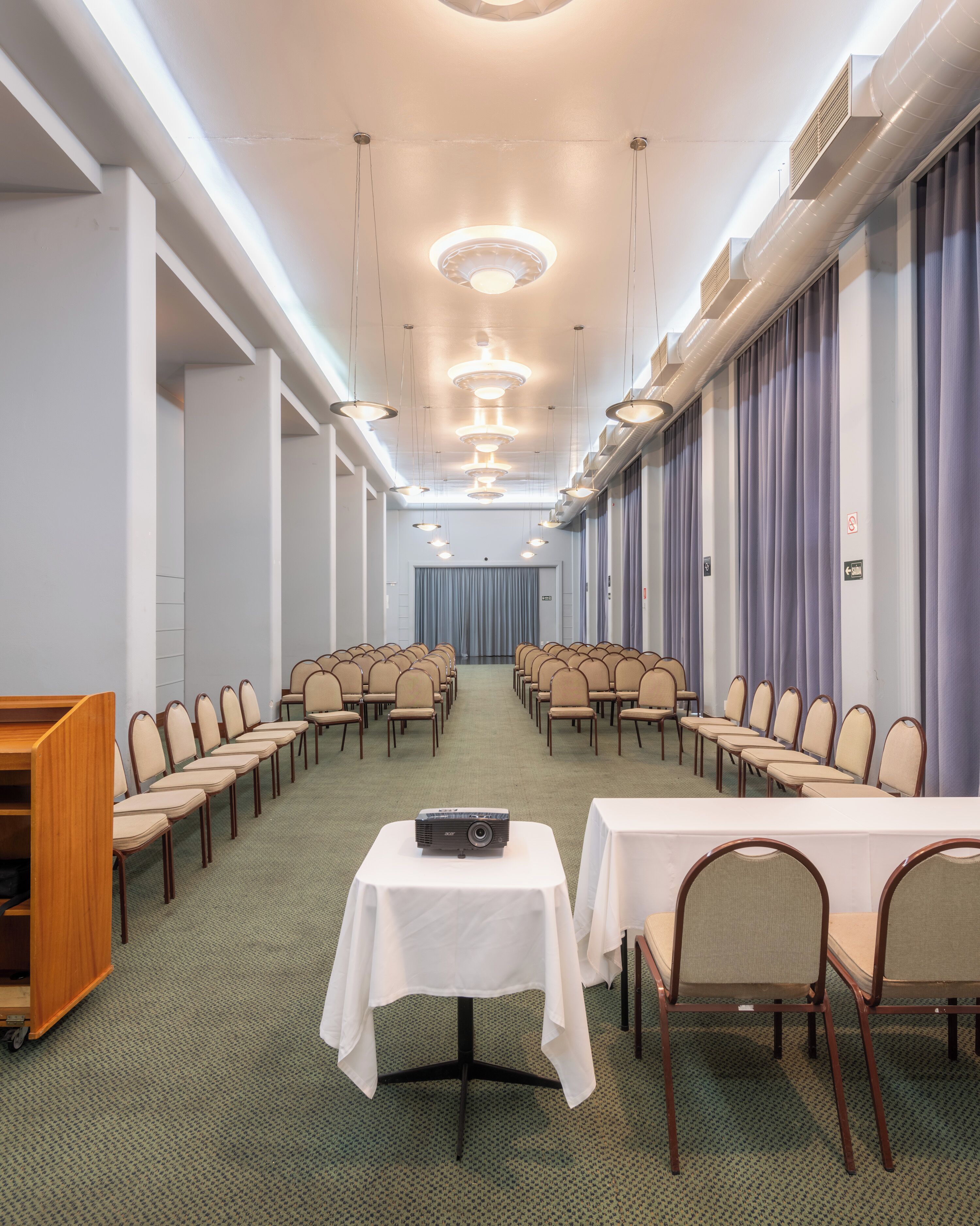 A conference room with rows of chairs, a projector on a table, and a long table with chairs.