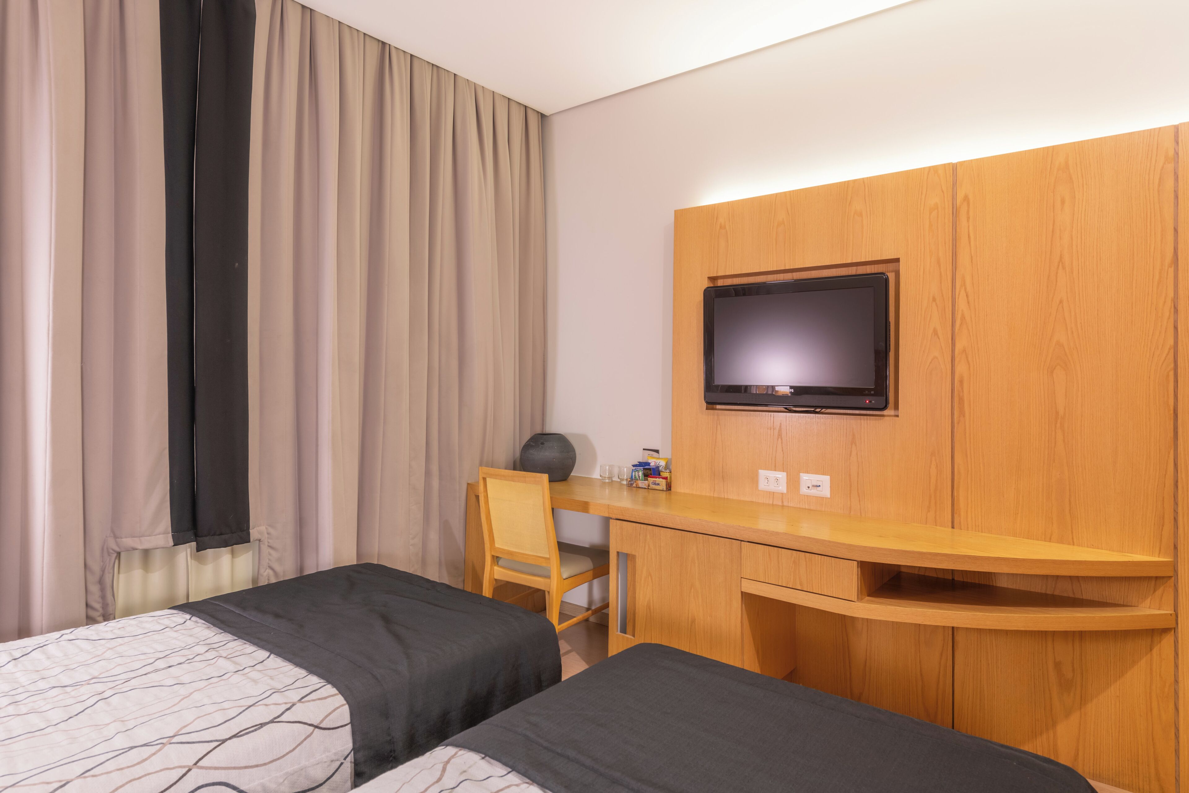 A hotel room with two beds, a desk, a chair, a television, and a window with curtains.