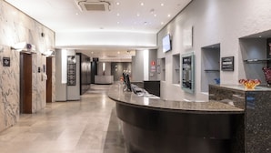 Un vestíbulo de hotel moderno con un mostrador de recepción curvo, suelo de mármol y una gran pantalla digital en la pared.
