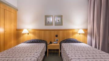 Una habitación de hotel con dos camas, un escritorio, un teléfono y dos cuadros en la pared.