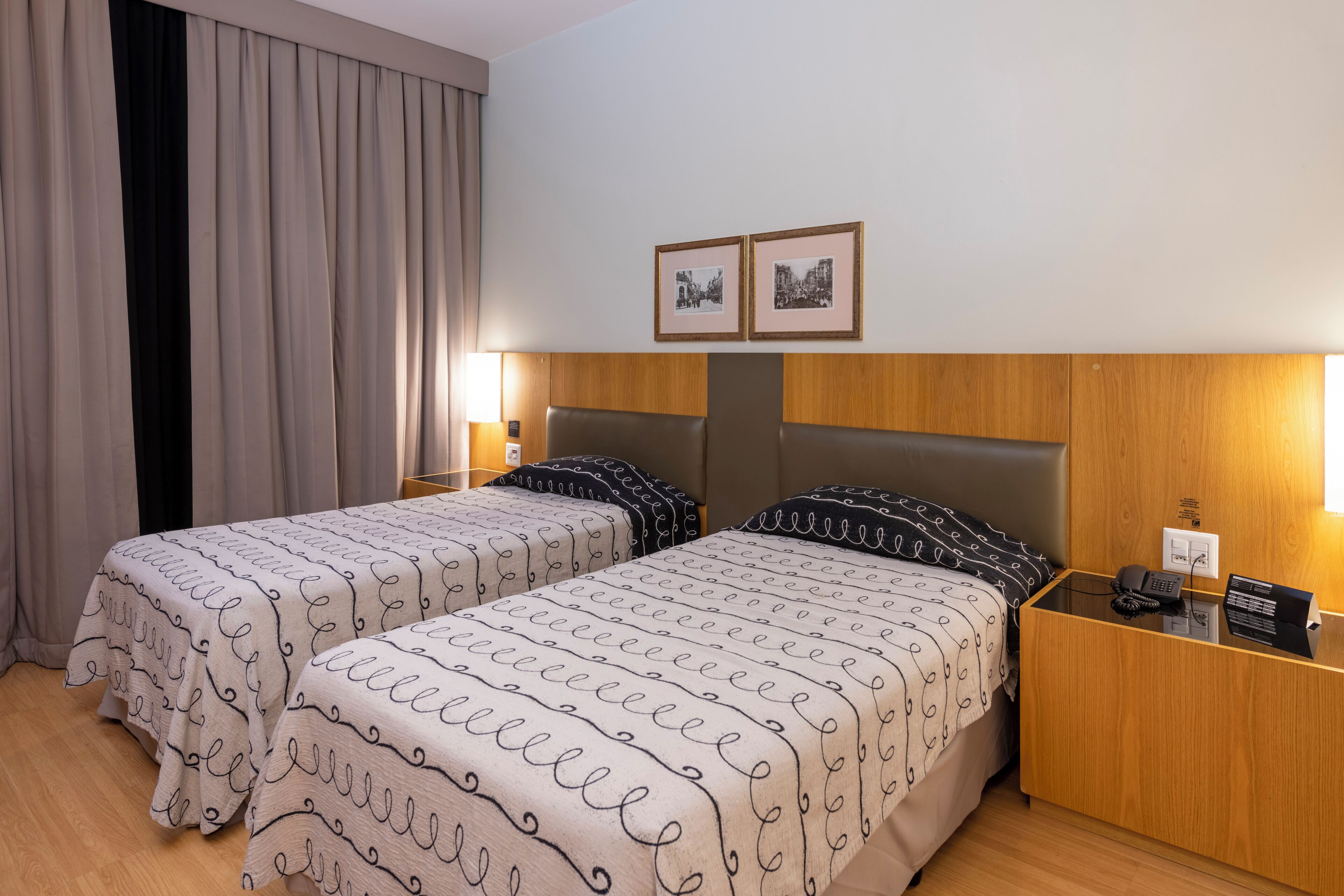 A hotel room with two beds, a wooden headboard, bedside tables with lamps, and framed pictures on the wall.
