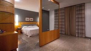 Una habitación de hotel moderna con un espejo grande, un armario de madera, una cama con ropa blanca, una mesita de noche y un cabecero con una lámpara.