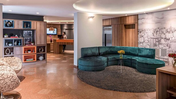 A modern living room with a curved sectional sofa, a round coffee table, and a cityscape mural on the wall. - Mercure Sao Paulo Alamedas (São Paulo)