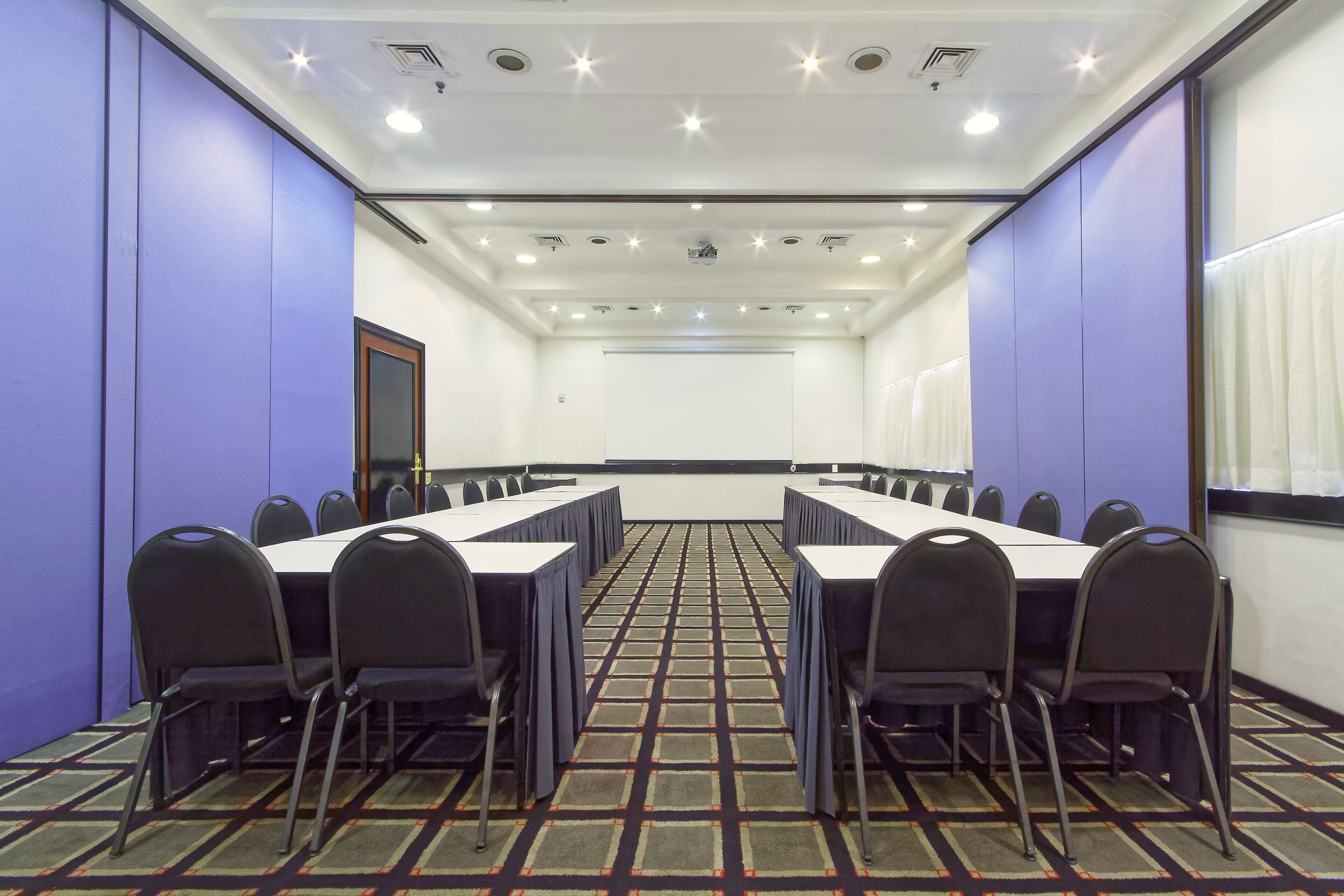 Una sala conferenze con un lungo tavolo e sedie, pareti bianche e un tappeto decorato.