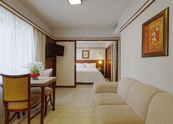 A hotel room with a bed, a TV, a dining area with a table and chairs, and a sofa.