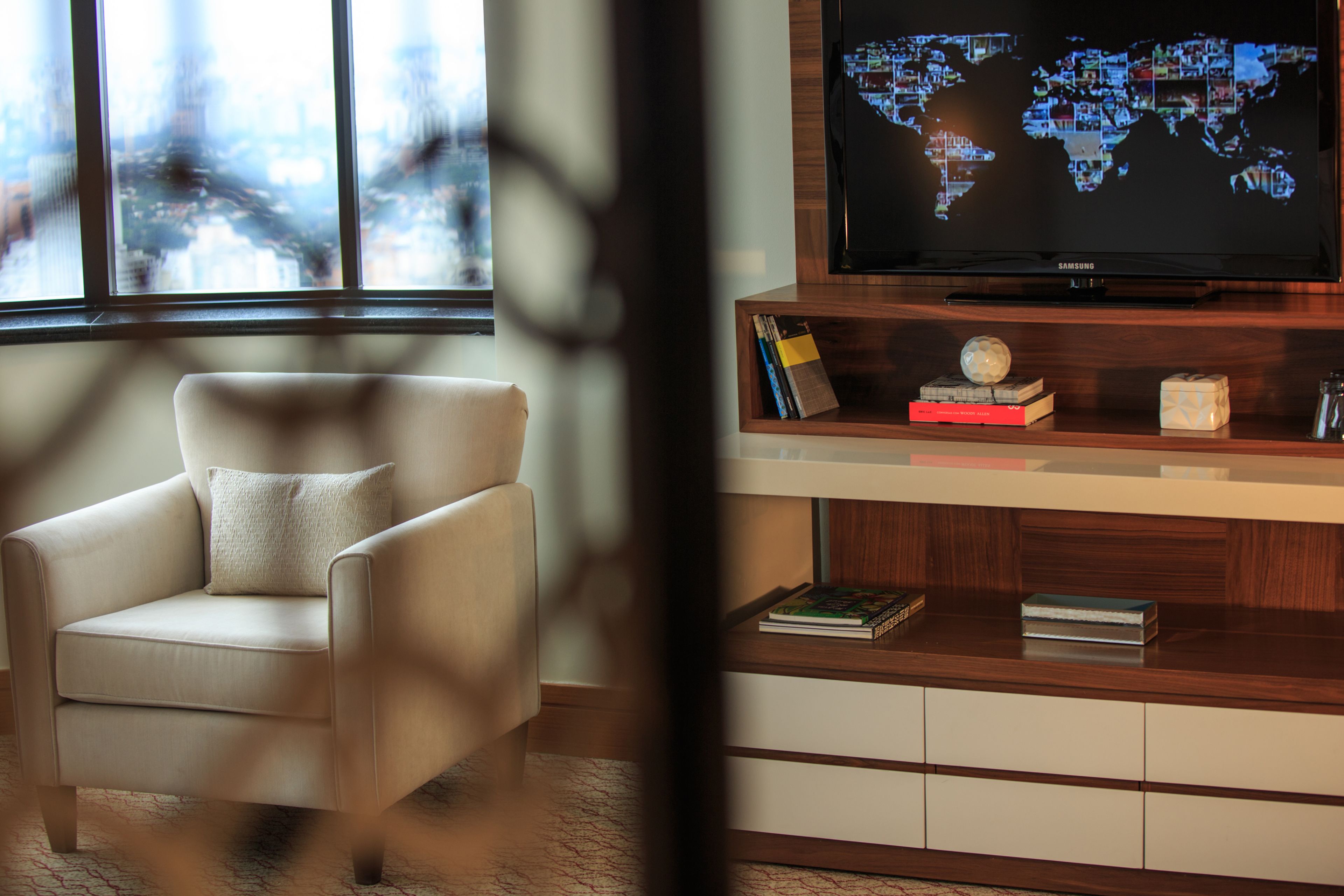 Ein modernes Wohnzimmer mit einem Ledersessel, einer Holz-Unterhaltungseinheit mit einem Flachbildfernseher, der eine Weltkarte zeigt, und einem Bücherregal mit Büchern und Dekoration.