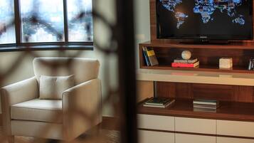 Ein modernes Wohnzimmer mit einem Ledersessel, einer Holz-Unterhaltungseinheit mit einem Flachbildfernseher, der eine Weltkarte zeigt, und einem Bücherregal mit Büchern und Dekoration.