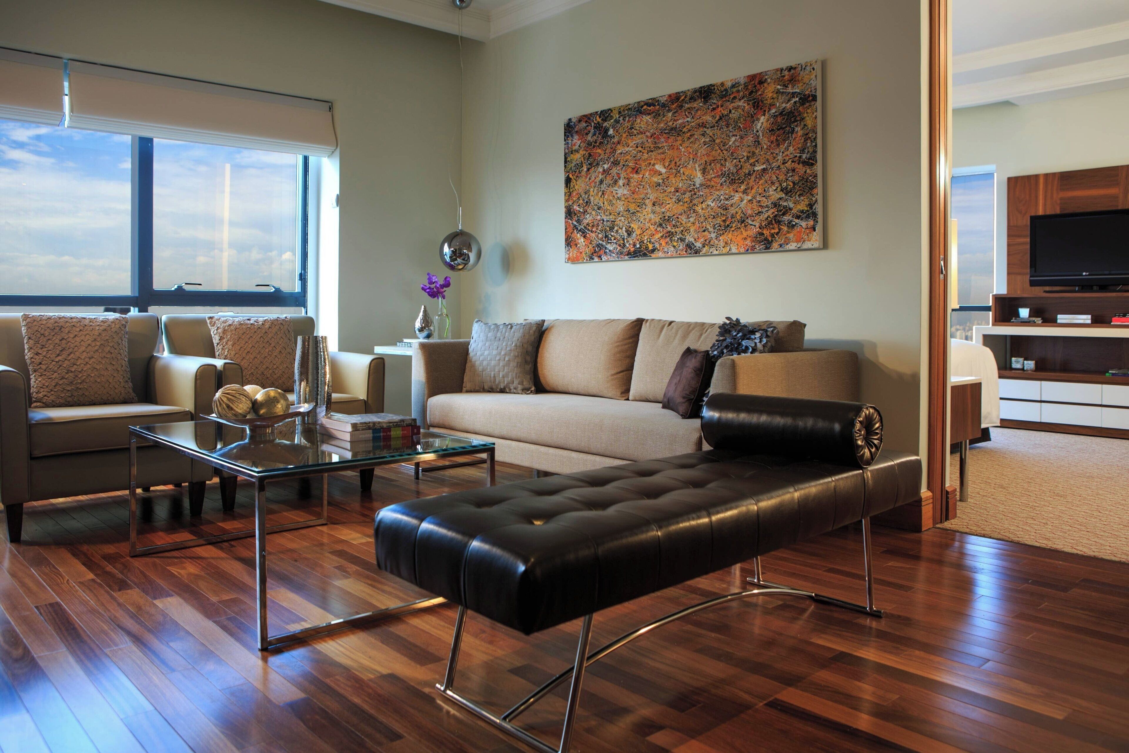 Una sala de estar moderna con un sofá, un reposapiés y una mesa de centro, un cuadro abstracto grande en la pared, y un televisor al fondo.