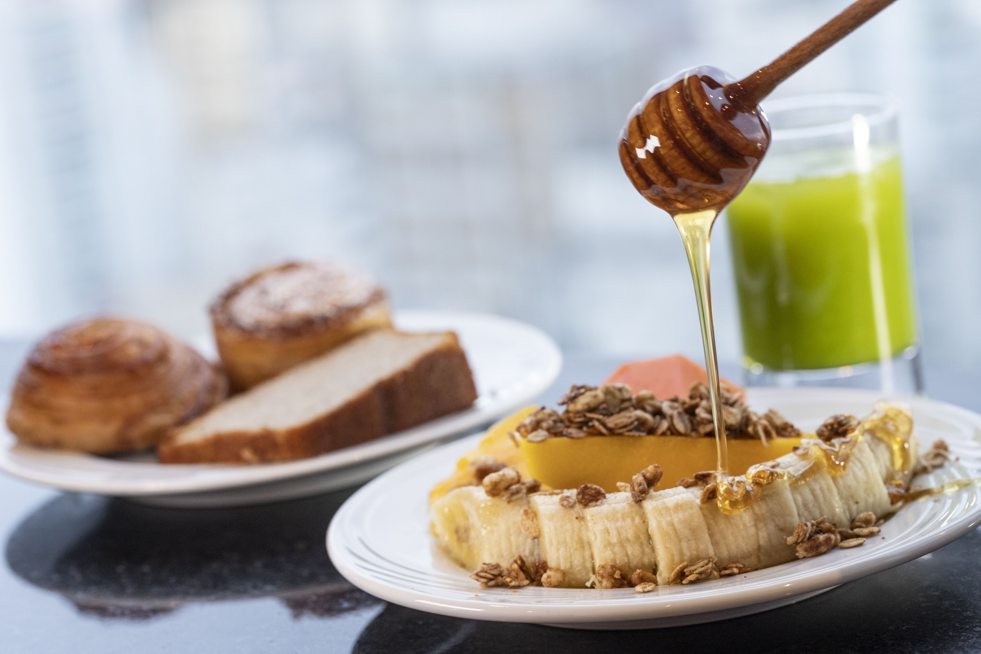 A breakfast plate with a banana, granola, and honey being drizzled on top.