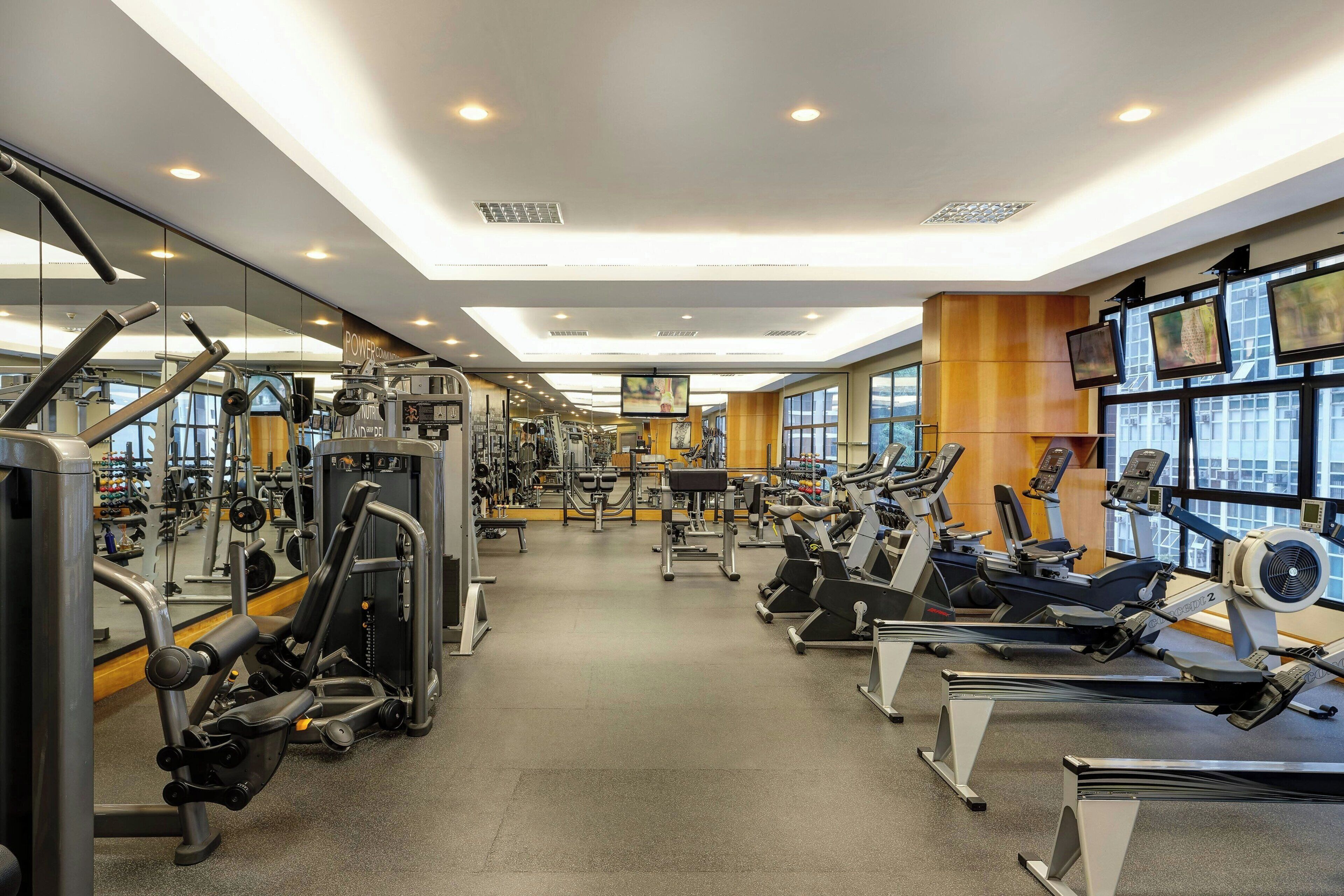 Un gimnasio con diversas máquinas de ejercicio, espejos y amplias ventanas.