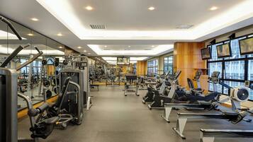 Un gimnasio con diversas máquinas de ejercicio, espejos y amplias ventanas.