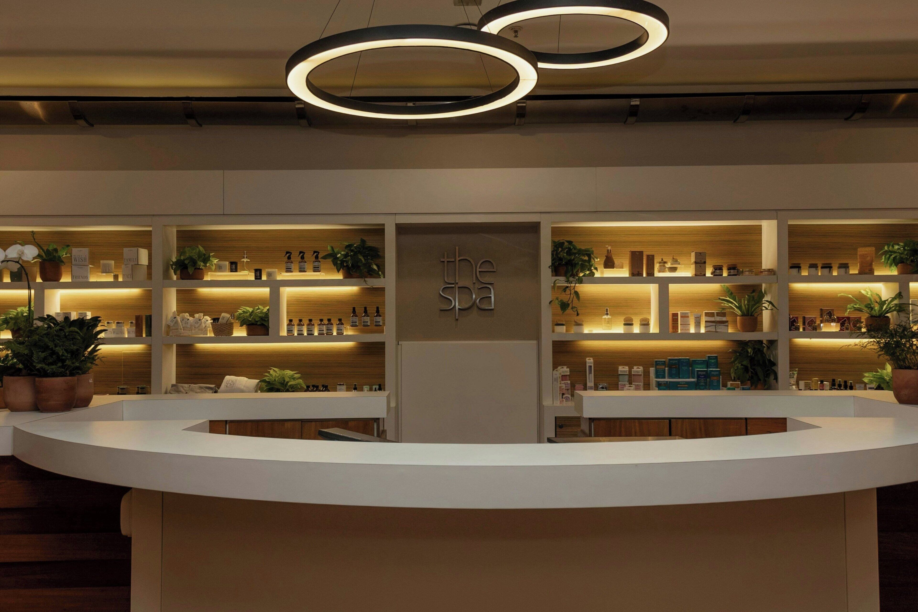 A reception area with a modern design, featuring a central counter, multiple shelves with products, and decorative plants.
