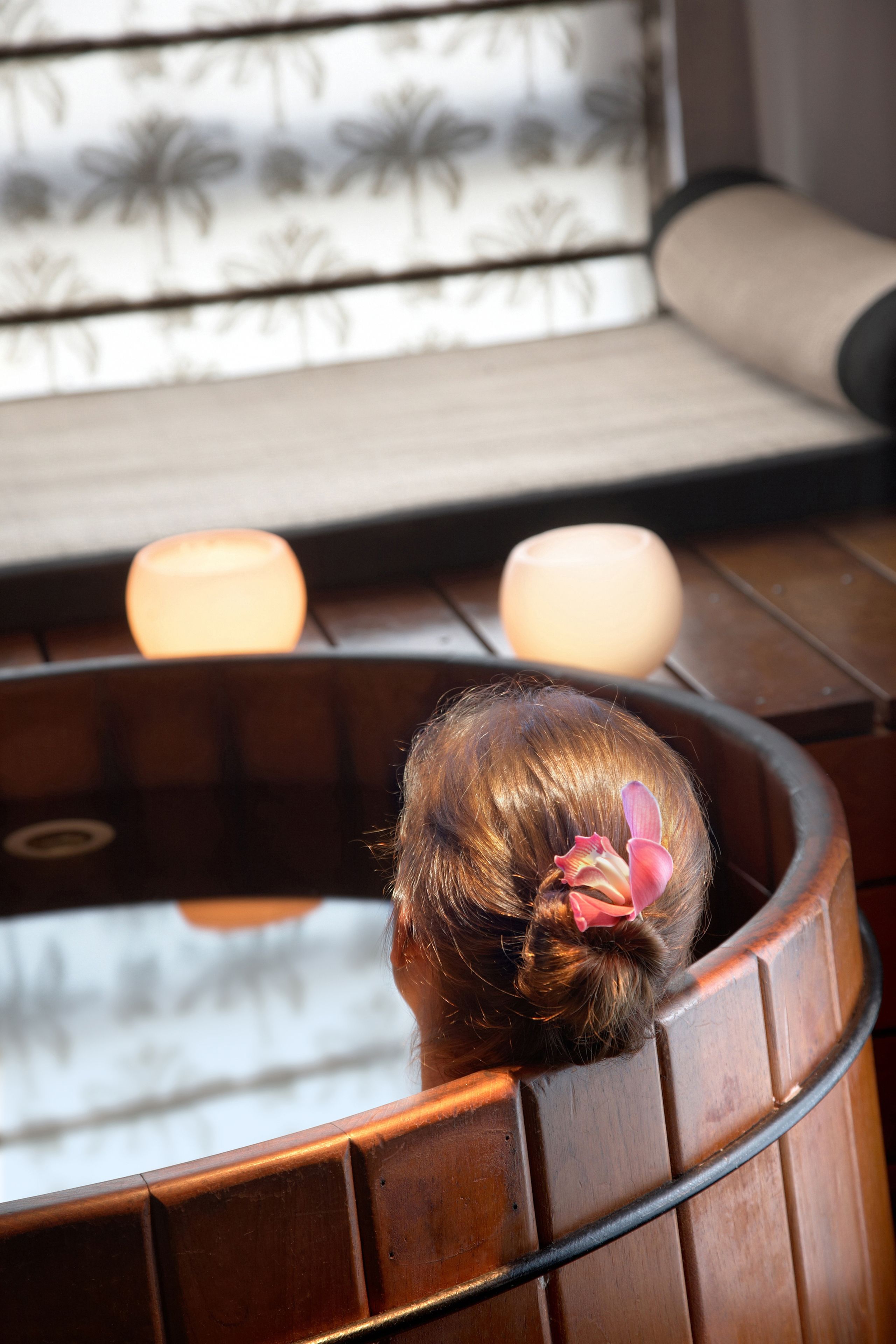 A bathtub with a wooden exterior and a glass interior, a towel, and a candle.