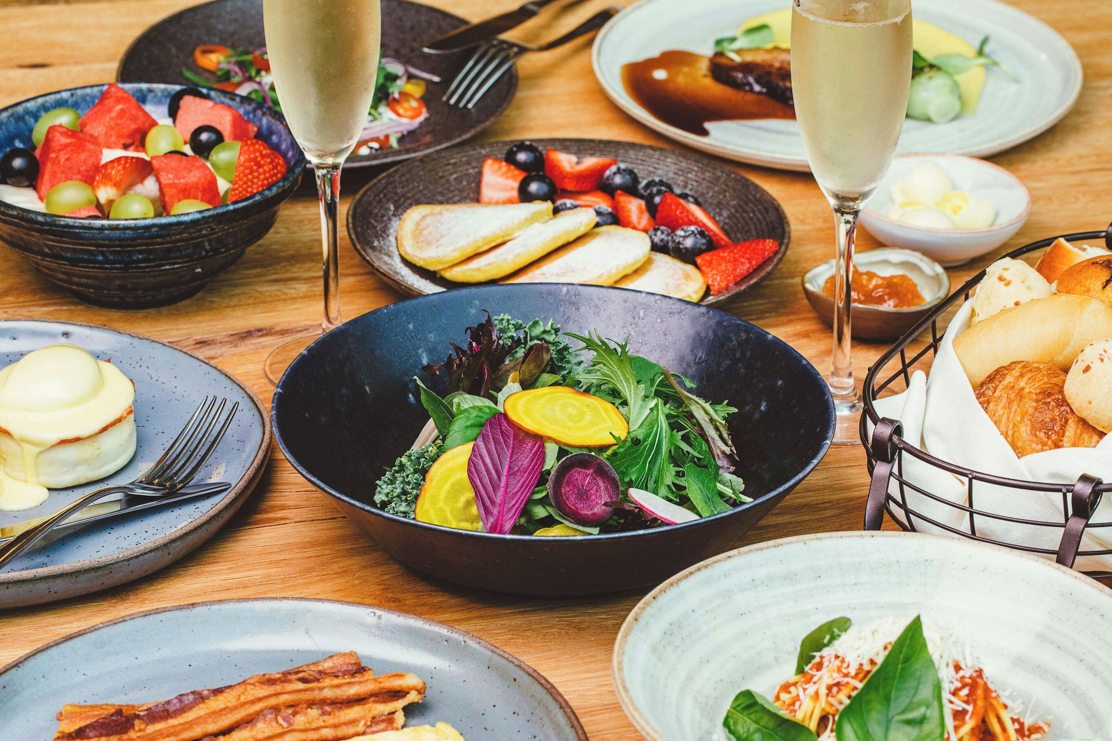 A variety of dishes including salads, fruits, and bread on a wooden table.