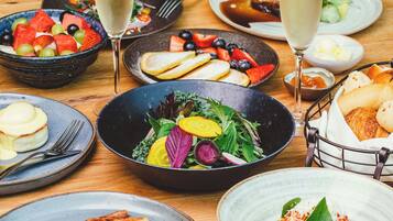 A variety of dishes including salads, fruits, and bread on a wooden table.