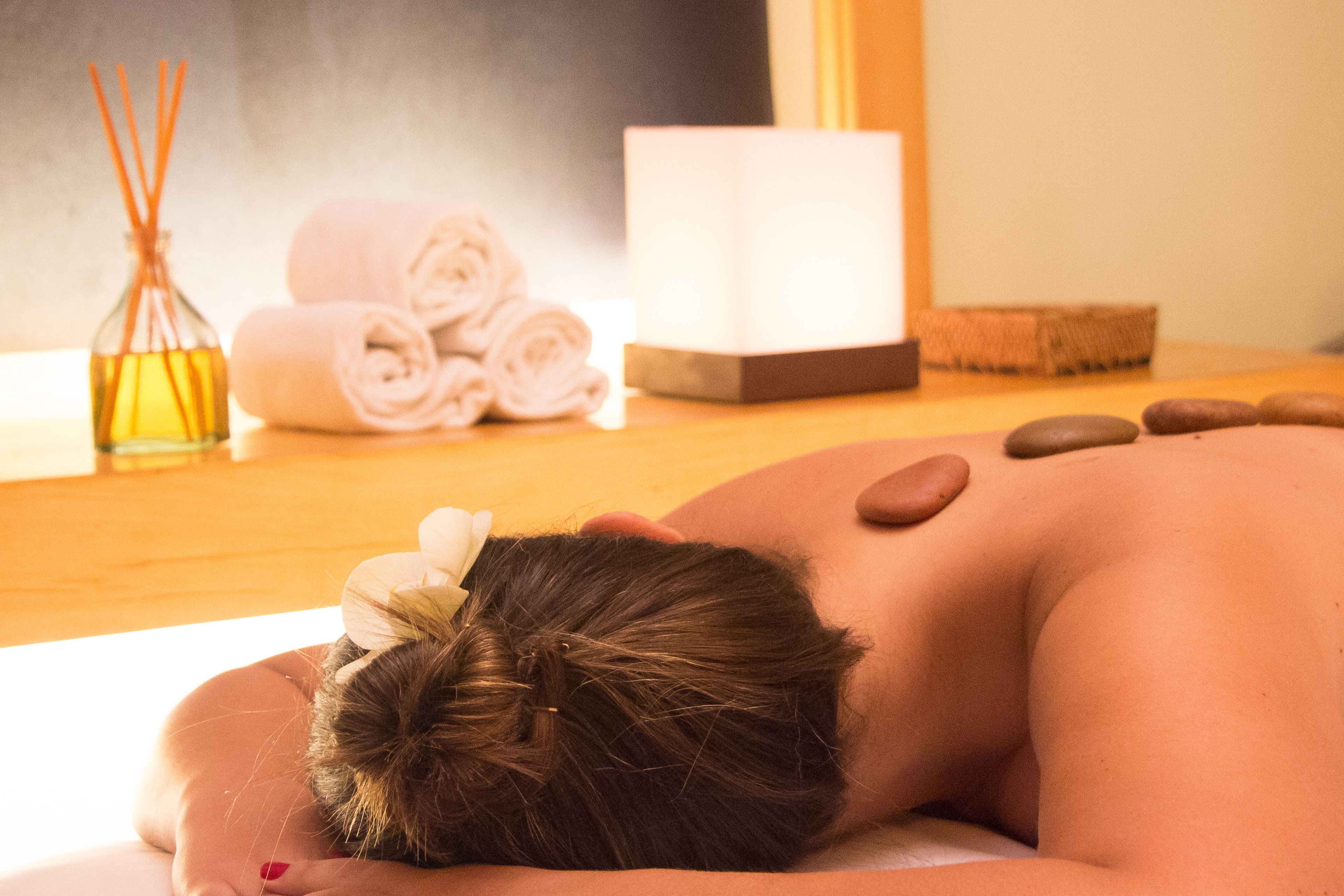 A person receiving a massage with a towel and a bottle of oil on a wooden table.