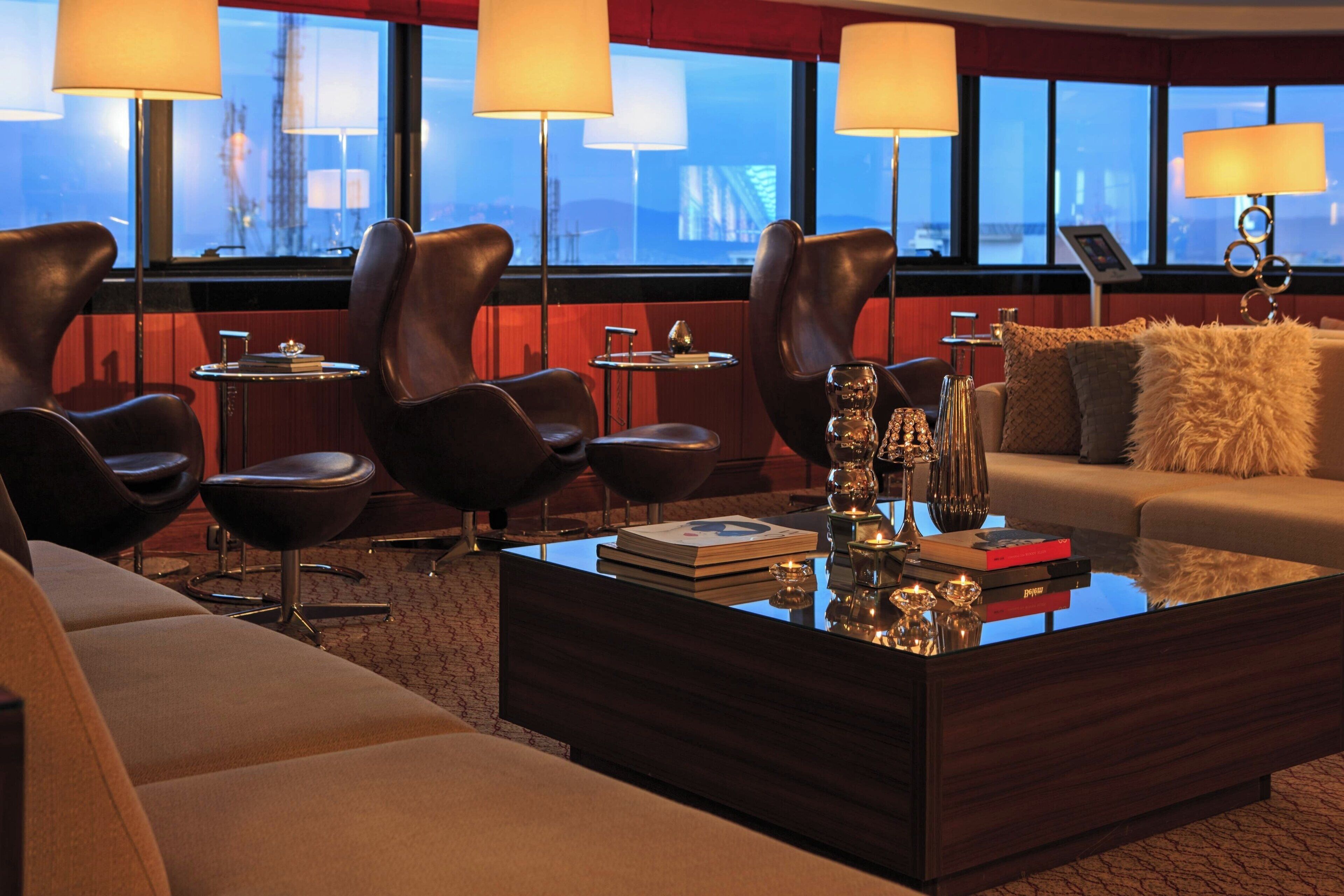 A modern hotel room with leather chairs, a glass coffee table, and a sofa.