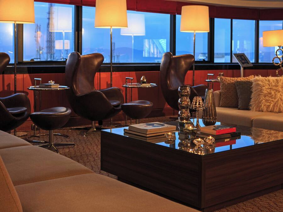 A modern hotel room with leather chairs, a glass coffee table, and a sofa.
