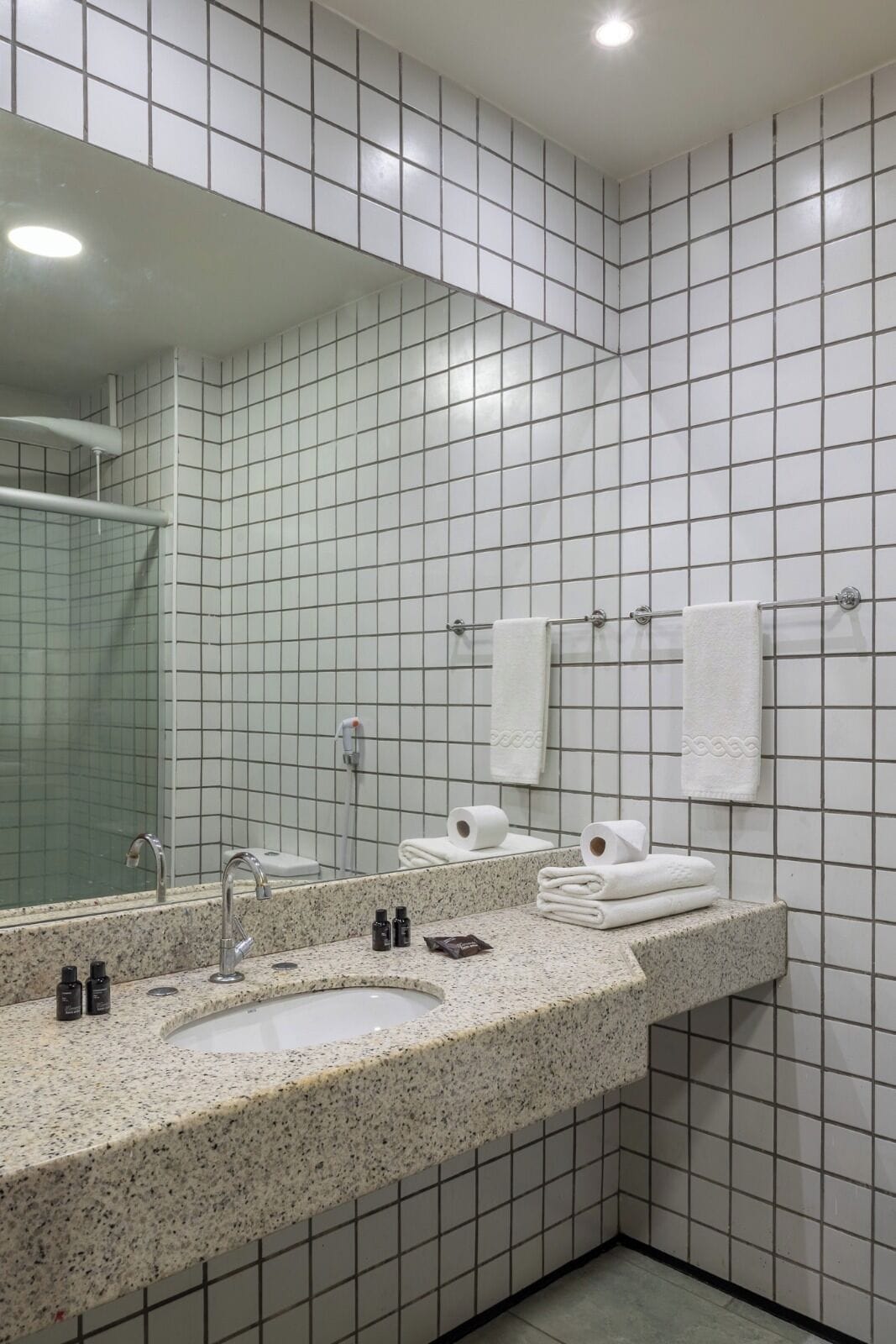 A modern bathroom with a granite countertop, two sinks, a large mirror, and white tiled walls.