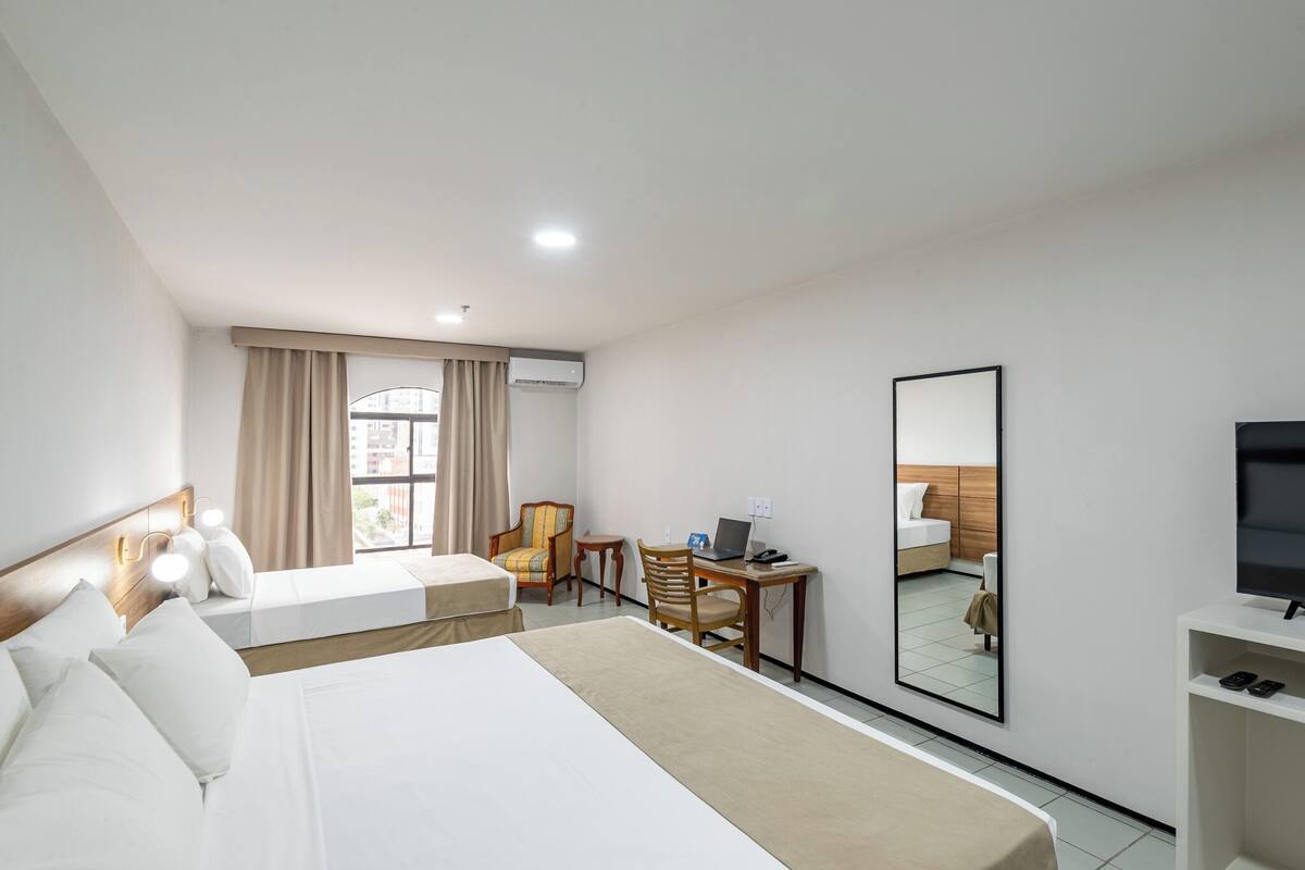 A hotel room with two beds, a desk with a laptop, a TV, and a mirror.