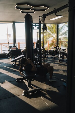 Uma academia com equipamentos de ginástica e vista para o oceano.