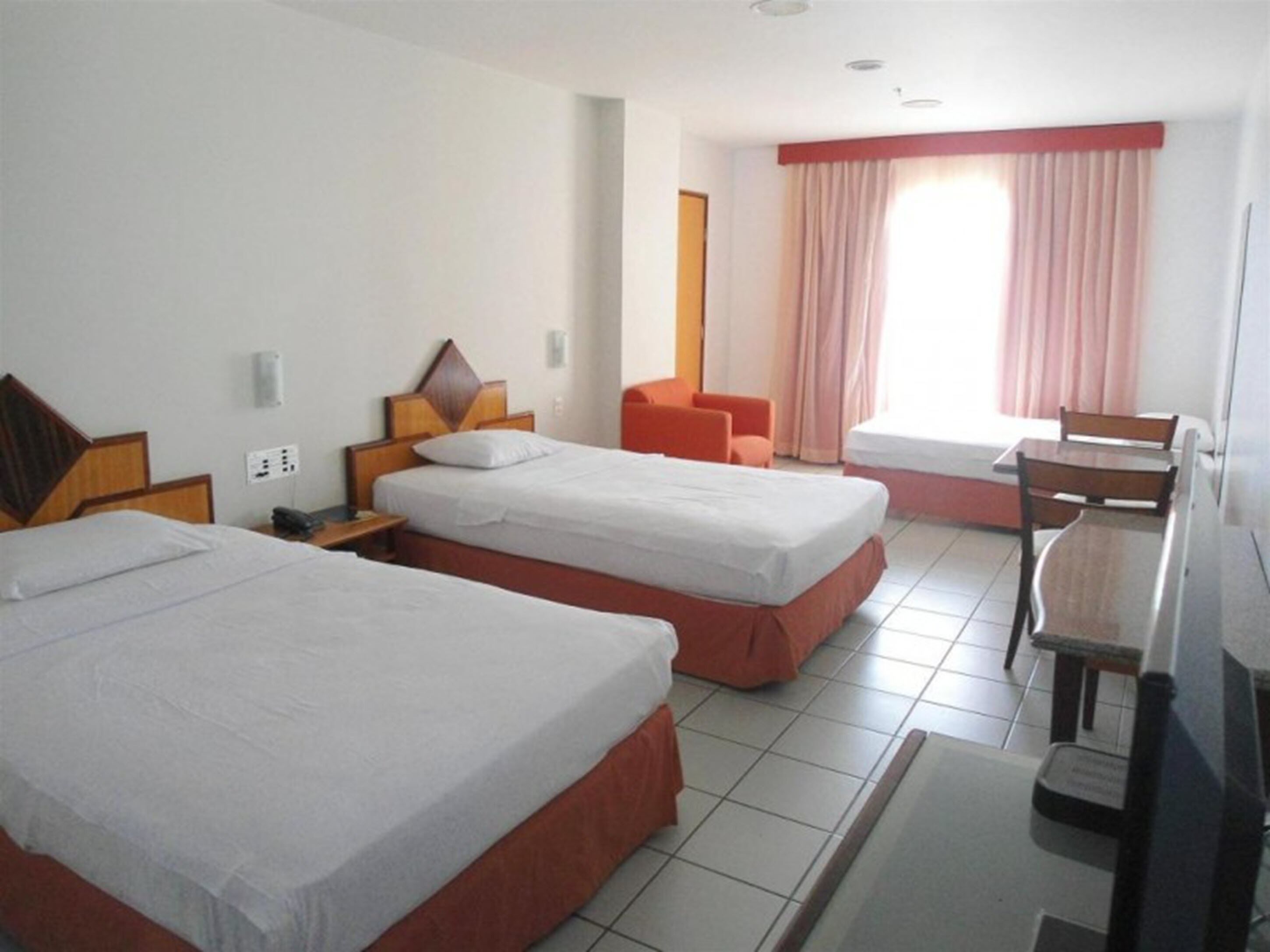 Habitación de hotel con dos camas individuales, un escritorio, una silla y una ventana con cortinas.