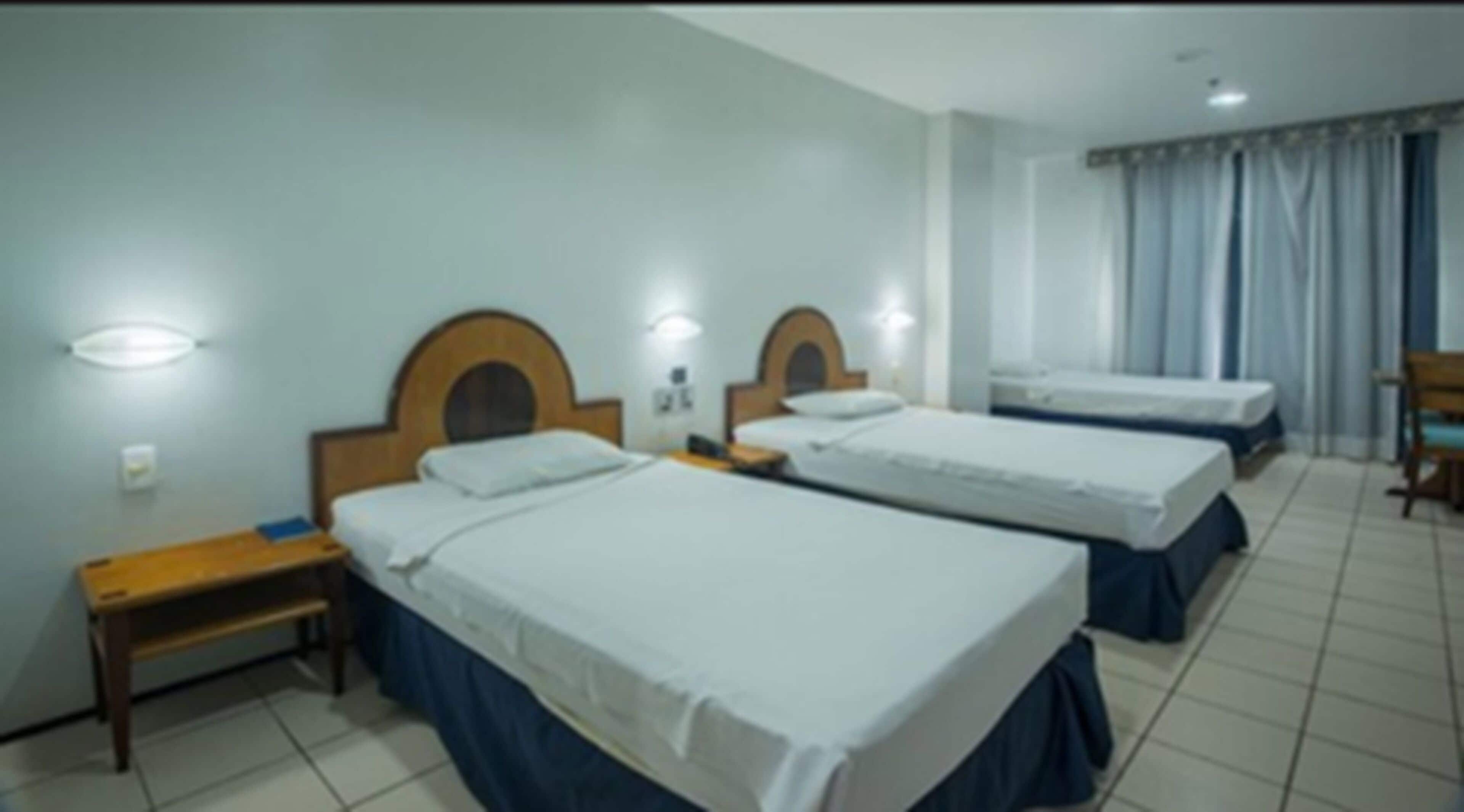 A hotel room with three single beds, wooden headboards, and bedside tables.