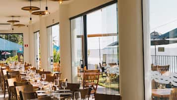 Un restaurante con varias mesas y sillas, ventanas amplias y lámparas colgantes.
